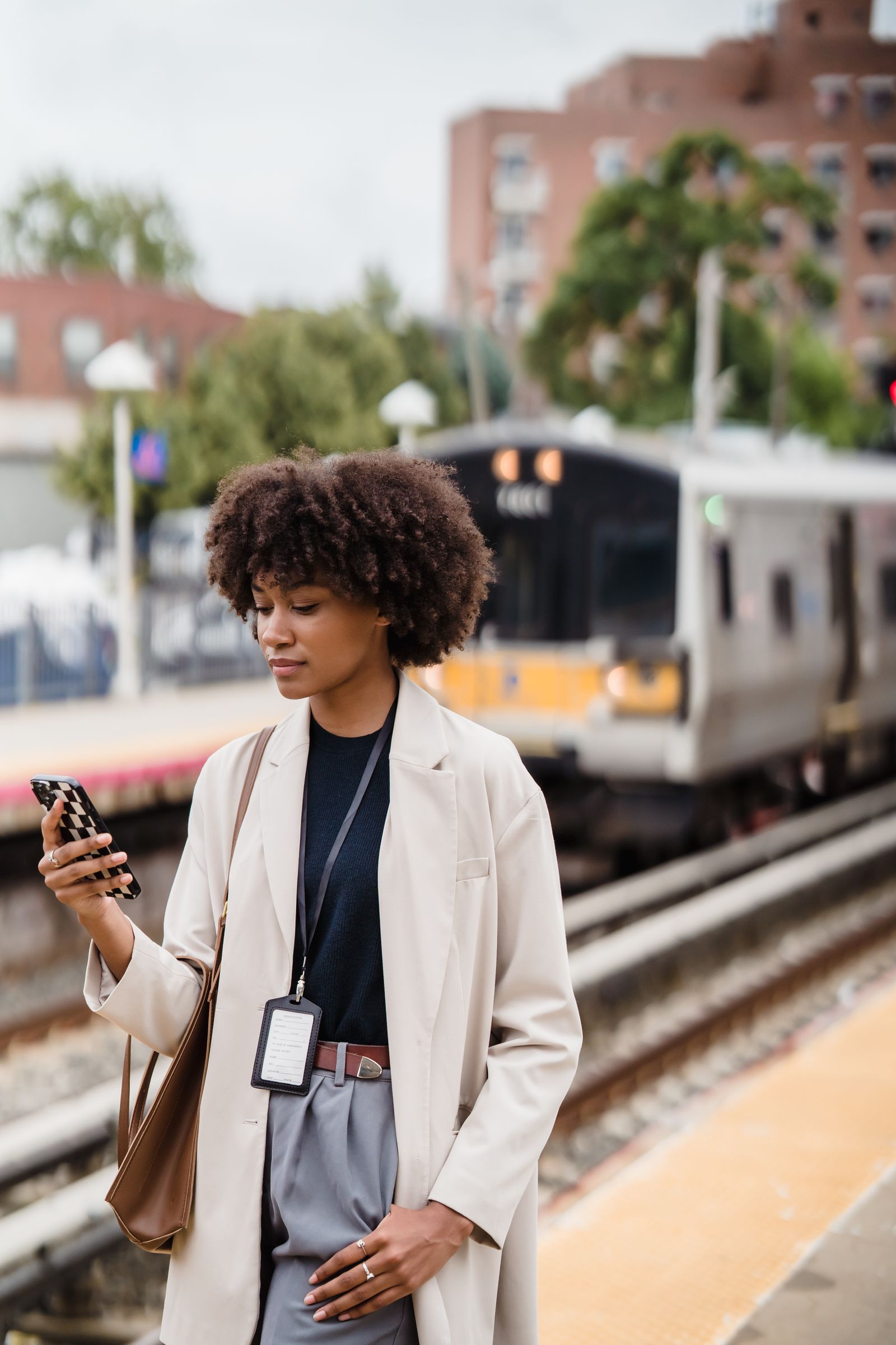 A young woman in a white blazer checks her phone on a train platform